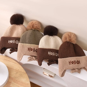 Close-up of knit winter earflap hats with fluffy pom-poms and 'Hello' smile embroidery