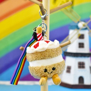 Close-up of a smiling cake plush keychain with a colorful rainbow strap pendant