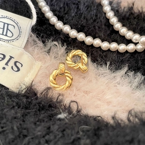 Detailed shot of gold-finished twisted rope hoop earrings resting on soft plush fabric