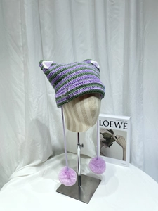 Detail of green and purple striped crochet cat ear hat with pom-poms and safety pin accents