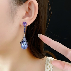 Macro shot of purple flower earrings with dangling blue gems and a drop pearl