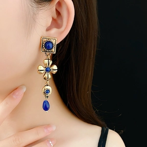 Detail view of vintage style gold earrings with blue gemstones worn by a model