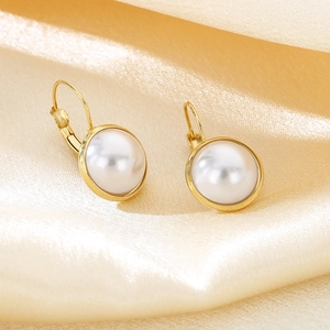 Detailed close-up of gold shell stud earrings on champagne silk fabric background