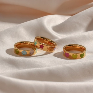 Three gold rings with colorful smile, star and heart designs on white silk fabric