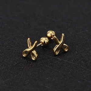 Detail view of golden scissor-shaped titanium steel ear studs on a black textured surface