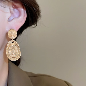 Close-up of gold drop earrings with textured spiral design worn by a female model
