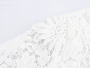 Detailed close-up of delicate white floral lace fabric with intricate mesh structure