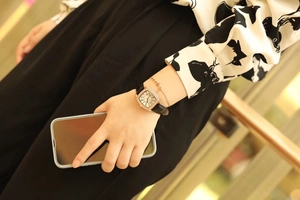 Close-up of a rose gold tonneau-shaped watch with diamond bezel and black leather strap
