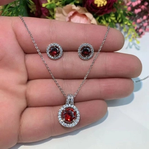 Detail showing hand holding silver necklace and earrings with red round zircon gemstones