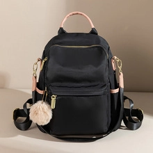 Detail of black nylon backpack featuring pink handles and a beige pompom zipper charm