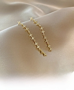 Detail of gold-tone long tassel earrings with star shapes and white zircon inlays