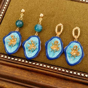 Detailed close-up of vintage gold earrings with blue enamel in a green velvet jewelry box