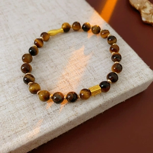 Gros plan d'un bracelet en œil de tigre avec breloques dorées sur présentoir beige
