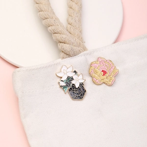 Detail of floral enamel brooches with lily and peony designs on a beige canvas bag