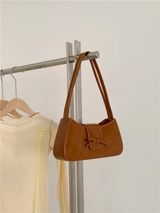 Brown PU leather baguette bag with a decorative bow hanging on a minimalist hanger
