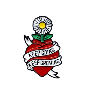 Detail of red heart enamel pin featuring daisy and Keep Going motivational text