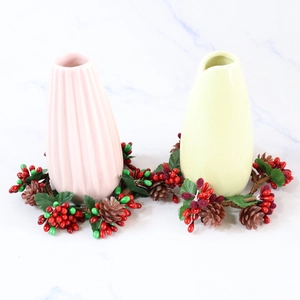 Roze en gele keramieken vazen met feestelijke dennenappelkransen op een marmeren ondergrond