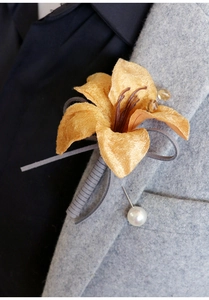 Detail of yellow lily boutonniere with velvet petals and pearl pin on a dark suit