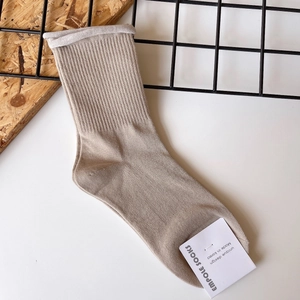 Detail of beige ribbed knit cotton socks featuring a rolled edge cuff and brand label