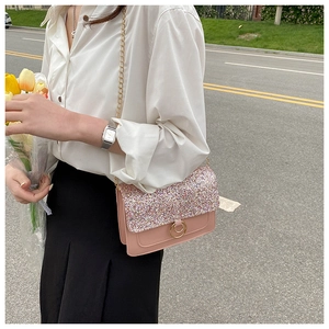 Pink sequin crossbody bag with chain strap and metal ring detail shown on a street model
