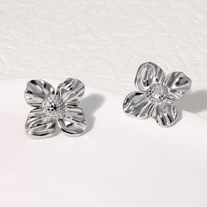 Macro detail of silver floral stud earrings featuring textured petals on white porcelain