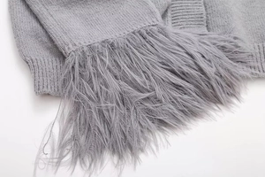 Makro-Detail des grauen Strickcardigans mit elegantem langen Fransenbesatz und Textur