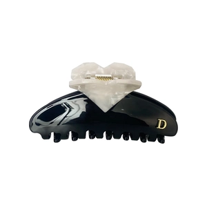 Detail of minimalist black and white hair claw with marble heart and golden letter D