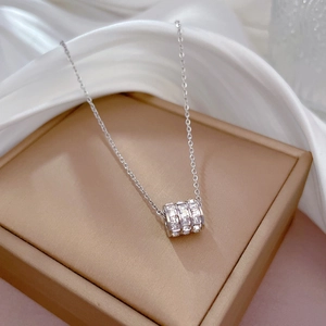 Detailed view of silver cylinder necklace with cubic zirconia on champagne silk gift box