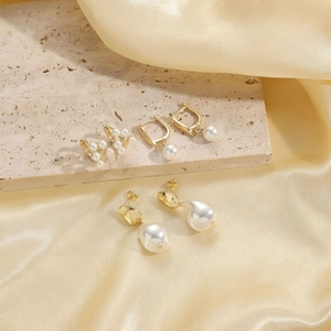 Detailed display of three elegant gold-plated pearl earrings on silk and stone background