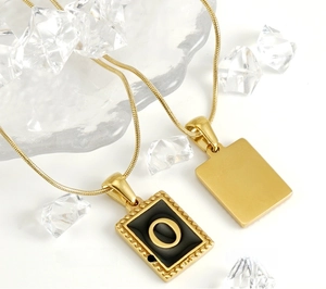 Detail of 18K gold snake chain necklace with square letter O shell pendant on ice