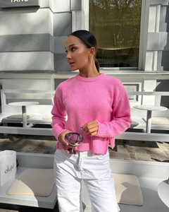 Detail of pink crewneck knit sweater hem showing side split and woven texture on model