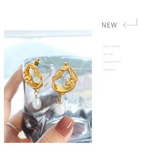 Detail view of gold lava irregular earrings with white pearl pendants on glass