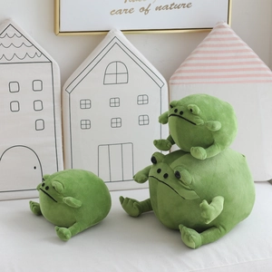 Cute green frog plush toys in various sizes stacked in a cozy, warm home setting