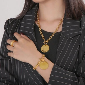 Close-up of polished gold O-chain necklace and bracelet set with round pendant on model