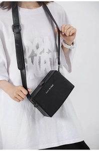 Detail view of the black box-shaped crossbody bag with a leather strap and brand logo