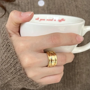 Close-up of a wide wave-textured gold ring styled with a cozy coffee cup and knit sweater