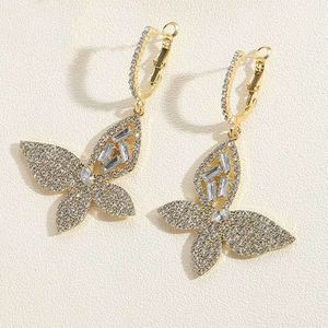 Detail of golden butterfly earrings featuring clear rhinestones on beige background