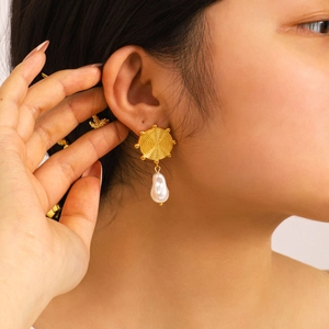 Gold plated stainless steel sunburst earrings with white baroque pearl drop on model