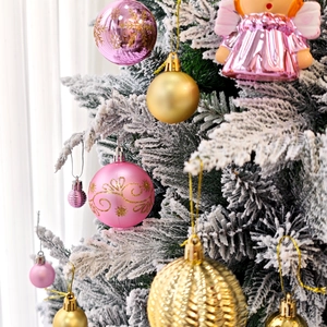 Gros plan de boules de Noël roses et dorées avec ange sur un sapin enneigé
