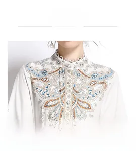Dettaglio della stampa paisley vintage e pizzo sullo scollo a V di un vestito bianco