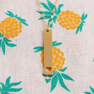 Nahaufnahme des goldenen Edelstahl-Rechteckanhängers mit Herz-Ausschnitt auf Ananas-Stoff