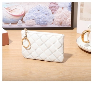 Close-up of white quilted PU leather coin purse with gold zipper and keyring on wood
