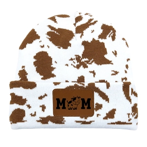 Macro detail of MOM leather patch on cow print knit beanie with sharp stitching texture