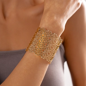 Dettaglio di un ampio bracciale rigido dorato a quadrifoglio indossato dal modello
