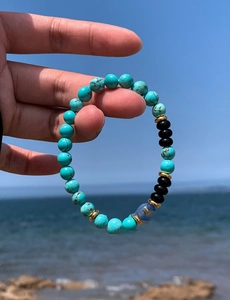 Close-up of turquoise and black beaded bracelet against a scenic blue ocean backdrop