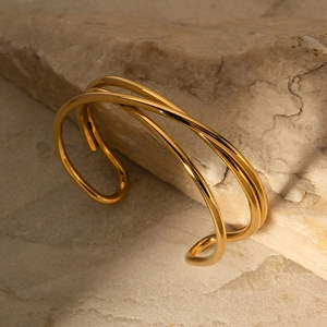 Detalle del brazalete abierto de acero inoxidable chapado en oro 18k con diseño cruzado