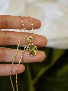 Macro detail of 18K gold necklace with olive green zircon and butterfly accents