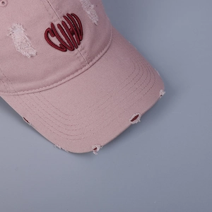 Vue détaillée de la casquette rose vieillie avec broderie CUPID rouge et bords effilochés