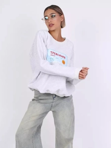Detail eines hellgrauen Rundhals-Sweatshirts mit russischem Text und Cartoon-Kuhdruck