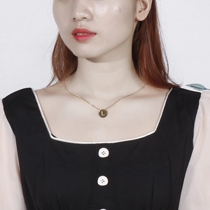 Close-up of golden necklace with round letter L pendant worn on collarbone